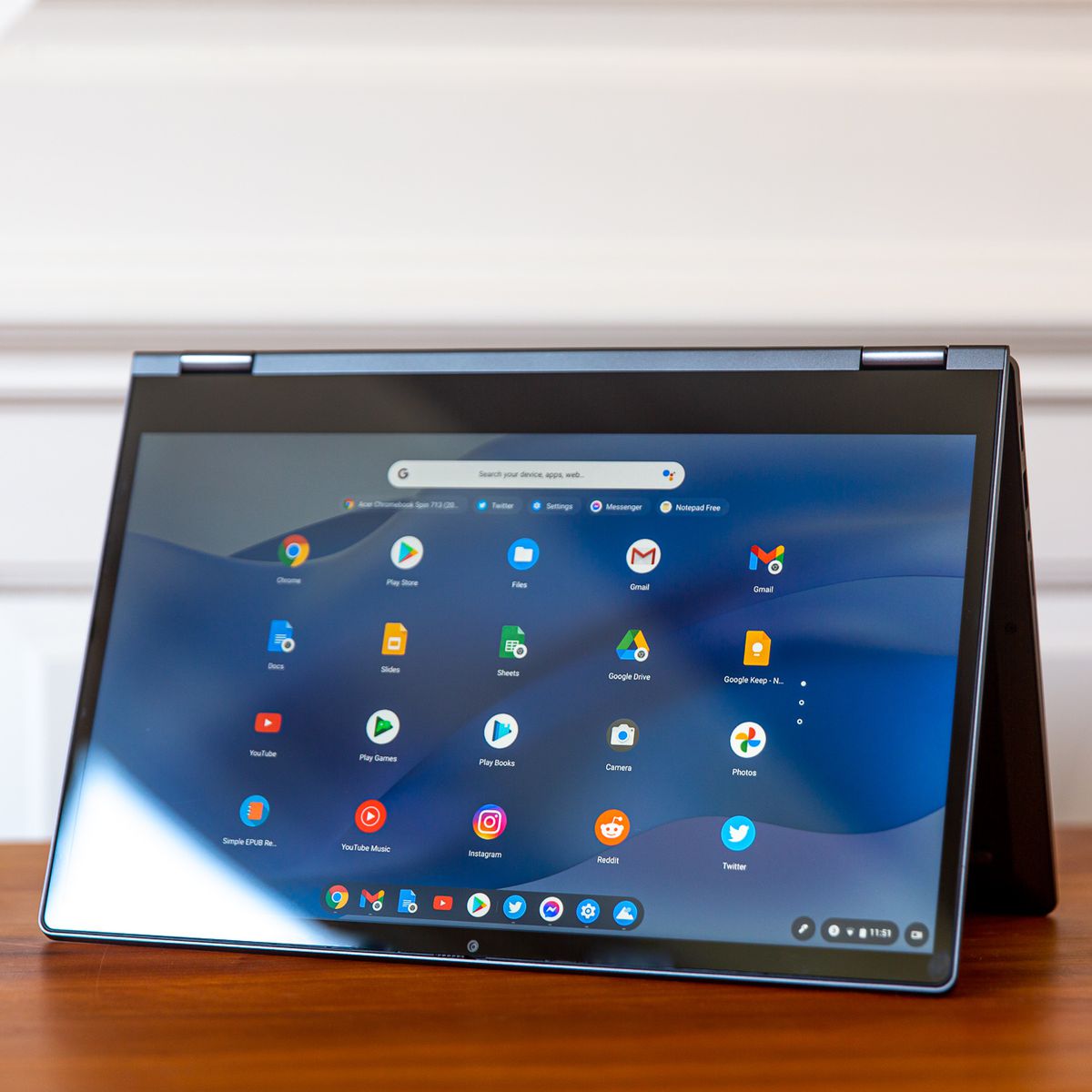 Das Lenovo Flex 5 Chromebook im Zeltmodus, nach links geneigt.  Auf dem Bildschirm wird ein Raster aus Chrome OS-Symbolen auf einem blauen, wellenförmigen Hintergrund angezeigt.
